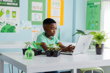 African American teenage male student wearing green tee working on laptop in class with plant pots