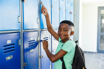 African American teenage male reaching up, unlocking blue lockers in school hallway with backpack