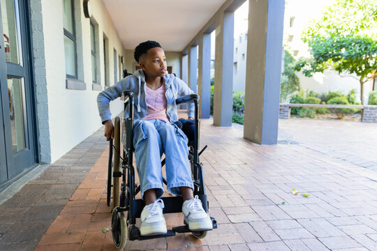 African American youth sitting in manual wheelchair on brick pavers by colonnade in grey hoodie