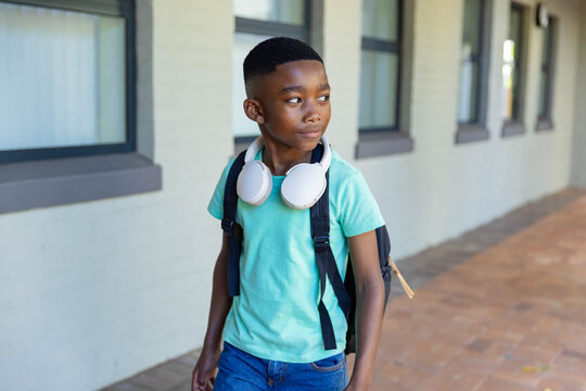 African-American child walking at school, wearing mint shirt, black backpack and white headphones