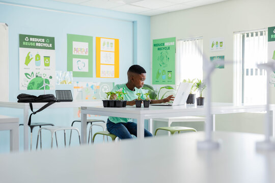 African American youth male studying plants and using laptop in classroom with solar panel