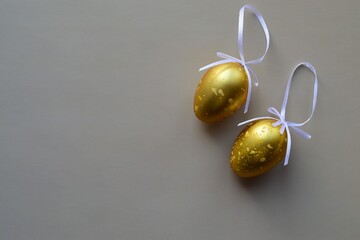 Two golden chicken eggs with ribbons on a dark background. Minimalistic Easter background
