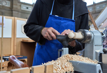 Close-up of a craftsman using a chisel to shape wood on a rotating lathe machine in a workshop....