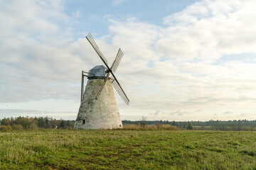 View of a weathered windmill stands tall against a backdrop of golden fields and a soft, cloud-strewn sky, evoking a sense of serene history, Lahemaa National Park, Estonia.