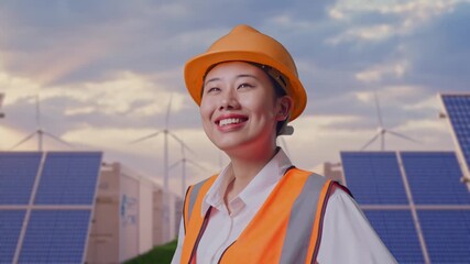 Close Up Side View Of Asian Female Engineer Wearing Safety Helmet Looking Around While Standing With Arms Akimbo at Energy Farm featuring Solar Panels, Battery Storage and Wind Turbines