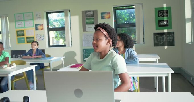 African American classmates watching preteen girl at front desk laptop smiling at passing teacher