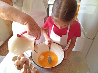 A grandmother and her granddaughter are making pancakes in the kitchen