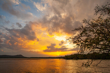 A breathtaking view of a colorful sunset reflecting on the calm surface of a lake, with vivid hues of orange, pink, and purple blending across the sky and water. The serene landscape evokes peace