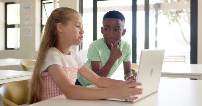 Diverse child peers girl initiating by typing, working at school desk with laptop for class project