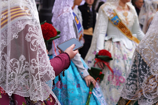 Fallas of Valencia. Faceless image of a group of falleras using a mobile phone, parading in traditional dress and carrying bouquets for the offering.