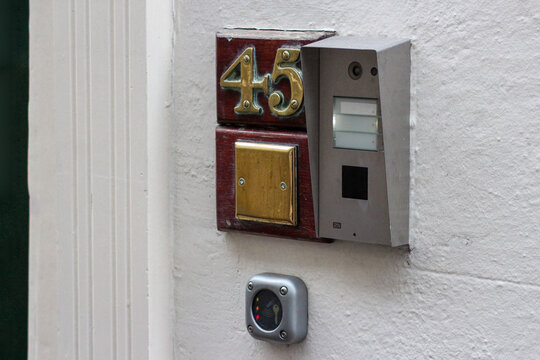A combination house number and access control system. Next to the house number is the intercom panel. Below it is a small metal device for access cards or key fobs used to enter the building.