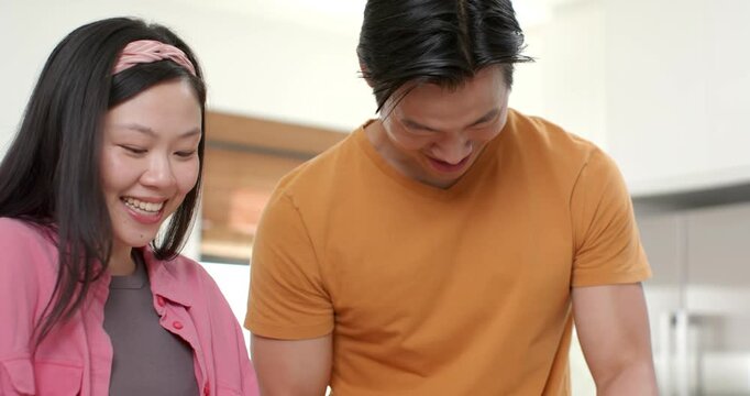 Diverse couple smiling then grinding mortar and peeling garlic in kitchen preparing meal