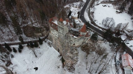 Obraz premium Aerial winter image of Bran Dracula Castle, the legendary Dracula fortress in Romania, drone view from above in fresh snow. The medieval Transylvania castle sits on a rocky hill. Travel background.