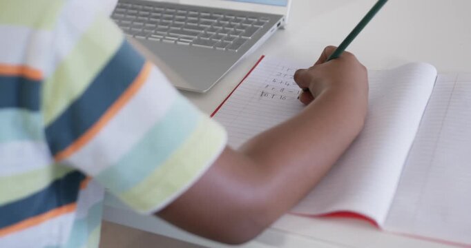 Child is placing pencil then writing math lines in lined notebook at white table, doing homework