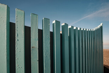 Obraz premium Close-up view of a curved fence made of vertical, closely spaced wooden pales, painted a light blue-green color on blue sky background