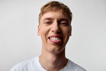 Smiling young man with tongue out, a playful expression and casual look in a studio shot with bright lighting against a white background, conveying fun, energy and youthful charm