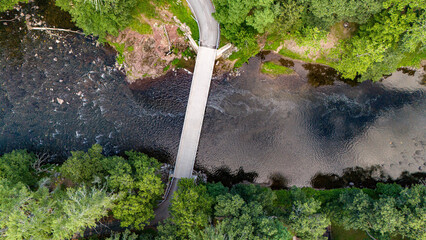 Aerial view of narrow bridge crossing river surrounded by dense green forest, top down drone landscape with road and flowing water