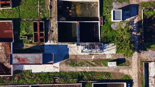 This hot day, workers are present at a large construction site with different types of structures and open ground. Machinery and tools are scattered around as work continues.