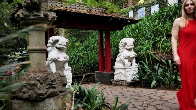 Fashionable individual walking along lush garden pathway with sculptures