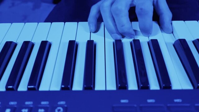 Male hands play a melody on an electronic piano keyboard. The scene is illuminated by vibrant blue and magenta neon lights, creating a modern, creative mood.