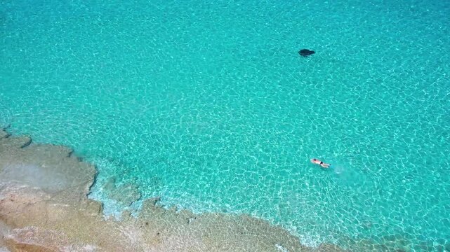 Aerial view of swimmer in turquoise crystal water at Kastani beach, Skopelos. Slow motion 60fps drone lift revealing yachts and Dassia island at Mamma Mia movie location. Greece