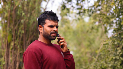 Young Indian man talking seriously on a mobile phone in a park with a green natural background.