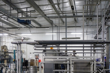 Interior of a beverage processing facility, featuring industrial machinery and extensive stainless steel process piping systems.