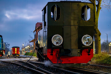 Historic steam locomotive stands on railway tracks at dusk at a railway station creating a calm historical atmosphere of the city
