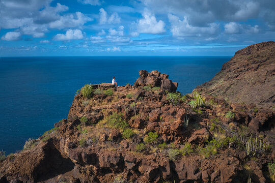 Female hiker resting on a rugged volcanic cliff above the Atlantic Ocean on La Palma, Canary Islands. Ideal for: adventure travel, hiking lifestyle, freedom concepts, outdoor inspiration and solo trav