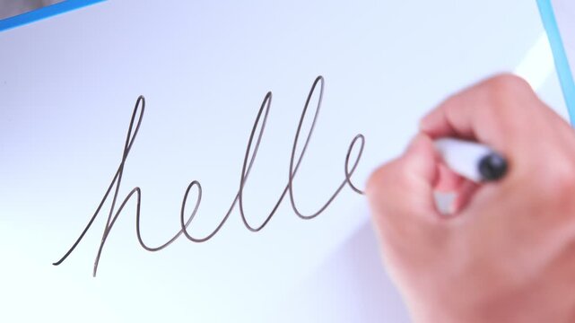 Person's hand writing the word hello in cursive on a white board with a black marker