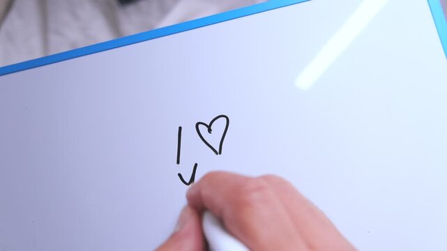 Person's hand writing the romantic message i love you with a black marker on a whiteboard