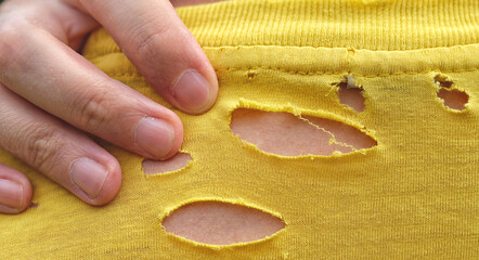 A close up shot of the back of a man wearing an old yellow t-shirt with holes in it. Close up.