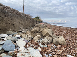 Coastal erosion exposes rocks and debris along rugged shoreline under cloudy sky