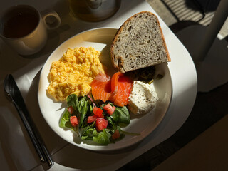 Simple breakfast with scrambled eggs, lightly salted fish, cream cheese, salad, and craft bread. Healthy food concept. Handmade smartphone photo, selective focus, harsh sunlight, non AI