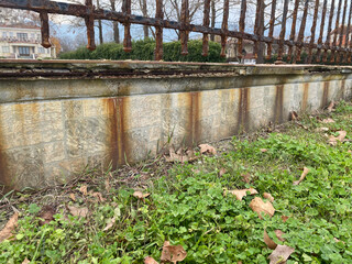 Rusty metal fence and weathered stone wall with grass and fallen leaves in outdoor setting