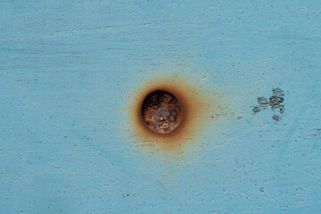 Close up of a rusted metal bolt embedded in a blue painted surface with visible corrosion marks and...