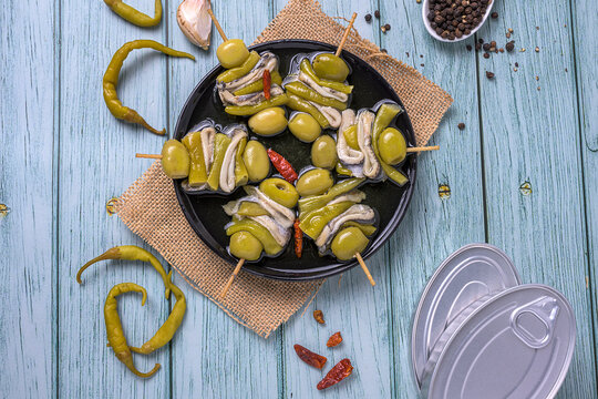Gildas appetizer with olives anchovies and peppers on a black plate over a blue wooden background