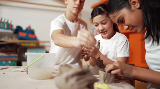 Clay piece placed on table while diverse happy children modeling cup. Diverse high school student playing or working with clay at pottery class or workshop. Creative activity or education. Edification