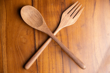 A pair of handcrafted wooden cutlery crossed on a natural wood surface. Top view of eco-friendly...