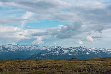 Dramatic top view to big snow-capped mountain range under rainy clouds in changeable weather. Scenic alpine landscape with sharp rocks, pointy peaks, peaked tops. Partly cloudy in high snowy mountains