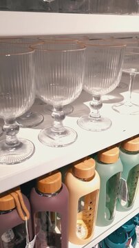 Elegant ribbed glass goblets and colorful reusable water bottles line store shelves. Camera pans slowly across the modern homeware products in a bright retail setting.