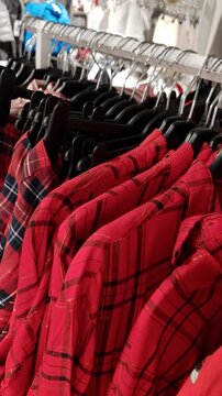 Red plaid shirts with gold thread accents hang in a row on black hangers. The camera pans slowly across the clothing rack in a brightly lit retail store.