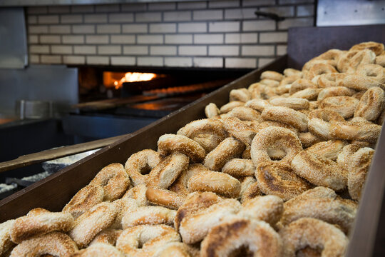 Sesame seed bagels in a metal bin at a bagel shop, oven in the background.