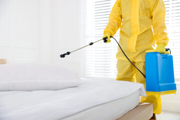 Pest control worker in protective suit spraying insecticide indoors, closeup