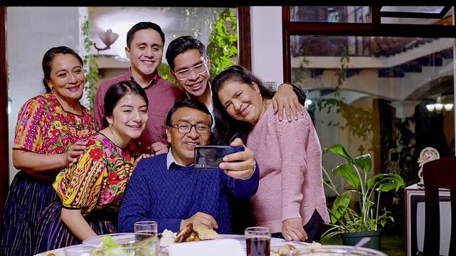 A Mayan family takes a photo during a celebratory dinner. The family smiles at the smartphone camera.