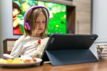 Child watching tablet at home with headphones while sitting at table during leisure time