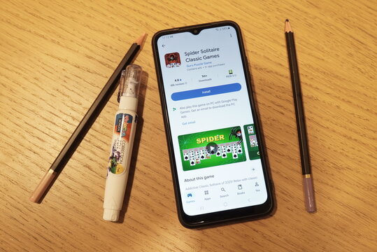 Smartphone displaying Spider Solitaire game app next to pencils and correction fluid