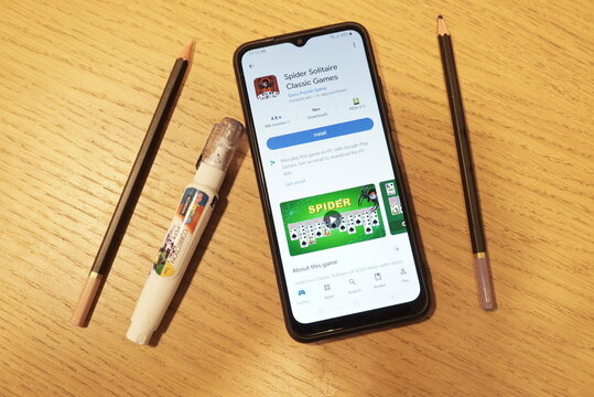 Smartphone displaying Spider Solitaire game app on wooden table with pencils