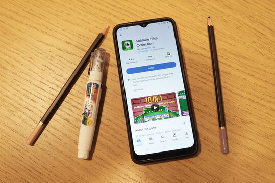 Smartphone displaying Solitaire Bliss Collection app page next to pencils and correction fluid