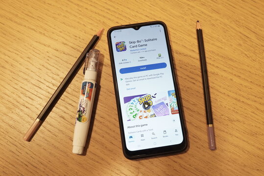 Smartphone displaying Skip-Bo Solitaire card game app page on wooden table